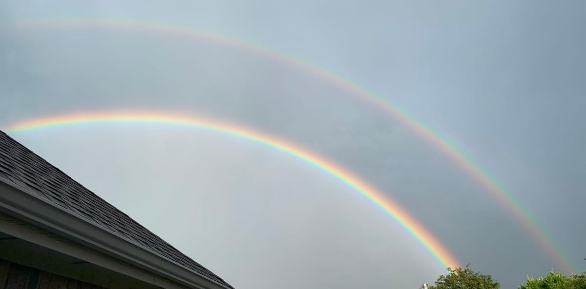 A double rainbow over a house. It almost looks like the sky is gray between the bows